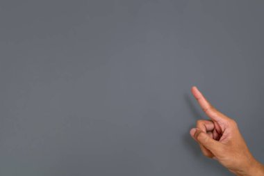 Gri arkaplandaki bir şeye işaret eden bir adamın eli ya da hareketi.