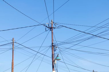 Mavi gökyüzü arka planlı elektrik direklerinin dağınık ve dağınık elektrik kabloları.