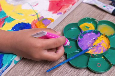 Küçük bir kızın eli suluboya paletine boya döküyor.