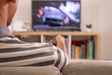 Asyalı bir adamın televizyon izlediği ve elinde uzaktan kumandayla eve geldiği arka plan.