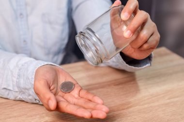 Bir kadın cam kavanozdan avucuna bozuk para döküyor. Yoksulluk kavramı.