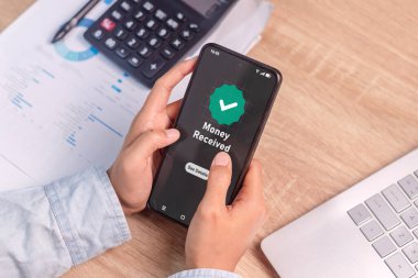 Alınan para mesajını gösteren telefon ekranlı akıllı telefonu tutan bir kadının eli. Çevrimiçi bankacılık veya nakit ödeme işlemi.