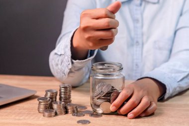 Bir kadın cam kavanoza bozuk para sayıp koyuyor. Tasarruf ve finansal konsept.