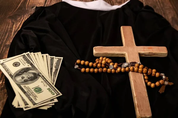 A Catholic cross, a rosary with beads and dollars lie on the black clothes of the priest before the service in the temple.