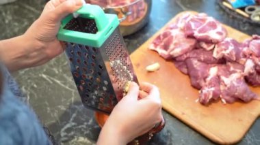 A woman in the kitchen grates garlic to add spices to meat.