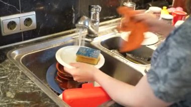 Woman housewife in the kitchen washes dirty dishes with hot water after eating.