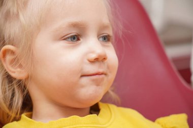 A little girl sits on a dental chair and waits for the doctor to get ready for work.