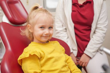 Little joyful girl sits on a dental chair after dental treatment.