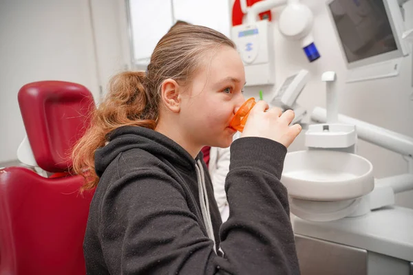 The girl rinses her mouth with water after examining and treating her teeth in the oral cavity at the dentist.