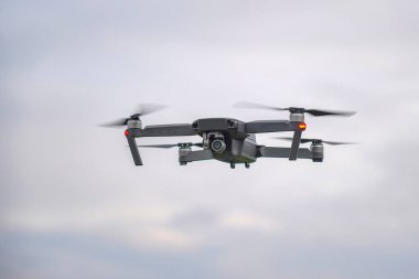 Bulutlu bir havada bulutlu bir gökyüzüne karşı uçan bir dron yeryüzünün yüzeyinin resimlerini çeker..