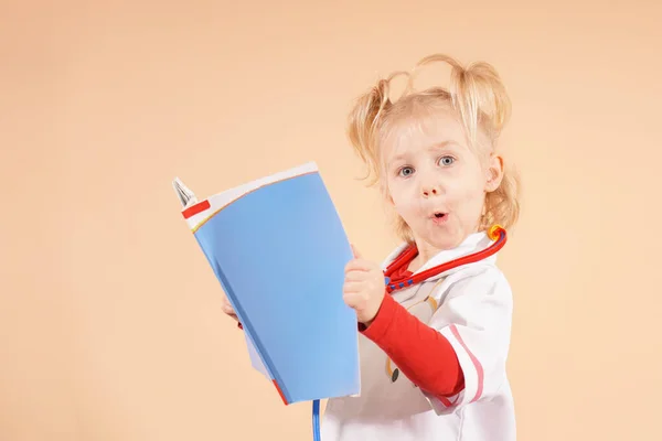 Mała Dziewczynka Stetoskopem Trzyma Książkę Rękach Patrzy Nią — Zdjęcie stockowe