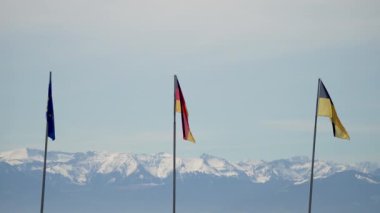 Alplerin arka planında üç bayrak dalgalanıyor. Birleşme kavramı, Avrupa Birliği, Ukrayna ve Almanya. Yüksek kalite 4k görüntü