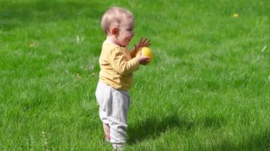 Küçük bir çocuk yeşil çimlerde ilk adımlarını atıyor. Çocuklar yürümeyi ve doğada oynamayı öğrenirler.. 