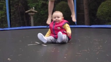 Küçük bir çocuk trambolinde oturur ve zıplar. Küçük çocuklar parkında eğlenmek ve oynamak. Yüksek kaliteli FullHD görüntüler