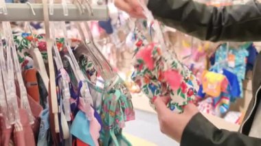 Bir kadın, alışveriş merkezindeki bir çocuk için yaz için çocuk mayosu seçer. Yüksek kaliteli FullHD görüntüler