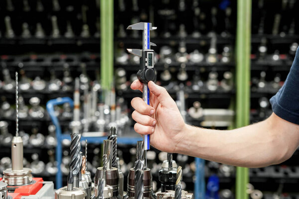 The worker operator of the cnc machine tool measures the cutting tool with a caliper for further work on milling and turning machines.