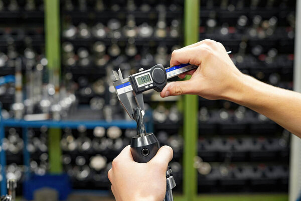 The worker operator of the cnc machine tool measures the cutting tool with a caliper for further work on milling and turning machines.