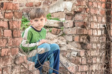 Zavallı ve mutsuz yetim çocuk, yıkılmış bir binanın yıkıntıları ve harabeleri üzerinde oturuyor. Sahnelenen fotoğraf.