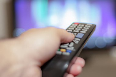 TV kumandalı bir kişi TV izlemek için kanal değiştirmek için uzaktan kumandayı kontrol eder.