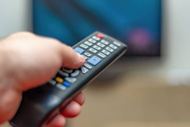 TV kumandalı bir kişi TV izlemek için kanal değiştirmek için uzaktan kumandayı kontrol eder.