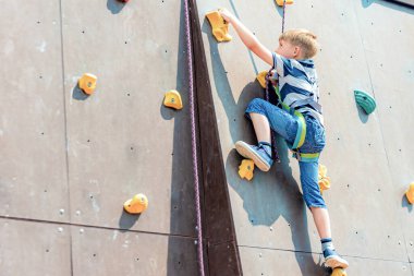 Tırmanma ekipmanları içinde bir çocuk, aşırı spor eğlence parkındaki tırmanışçılar için yapay bir kulenin tepesini fethediyor..
