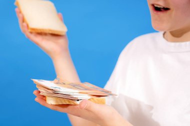 The girl made a burger from bread and banknotes and is trying to eat it. clipart
