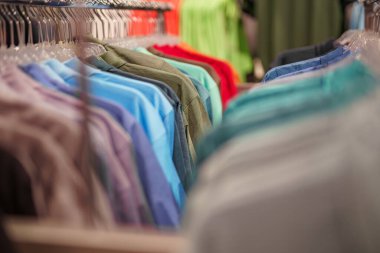 Alışveriş merkezinde satılık bir askıda farklı renklerde kazaklar ve tişörtler var..