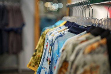 Alışveriş merkezinde satılık bir askıda farklı renklerde kazaklar ve tişörtler var..