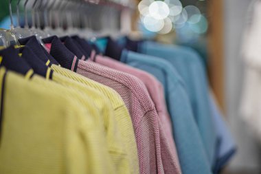 Alışveriş merkezinde satılık bir askıda farklı renklerde kazaklar ve tişörtler var..