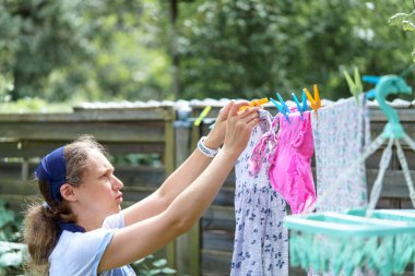 Bir kadın dışarıda kurutmak için bebek çamaşırlarını asıyor. Yıkandıktan sonra temiz çamaşır.