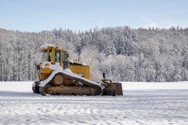 Sarı buldozer karlı bir ormanın arka planında.