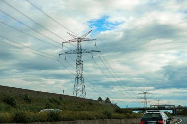 Akşam bulutlu gökyüzünün arka planında elektrik kabloları olan yüksek voltaj direği.