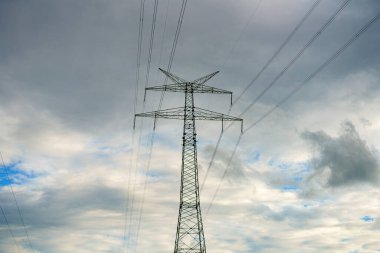 Akşam bulutlu gökyüzünün arka planında elektrik kabloları olan yüksek voltaj direği.