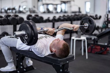 Spor salonunda triseps egzersizi yapan bir adam bir bankta EZ-halterle..