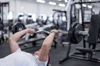 Spor salonunda triseps egzersizi yapan bir adam bir bankta EZ-halterle..