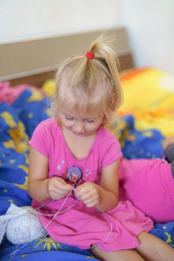 Küçük bir kız örgü iğneleriyle örüyor.