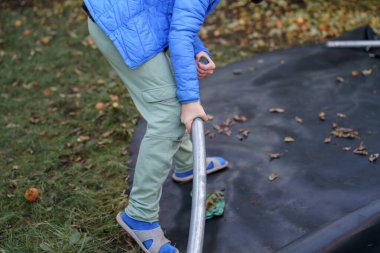 Çocuklar parçalanmış trambolin çerçevesini depolamak için taşırlar..