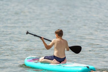 Çocuk şişme bir tahtaya biniyor ve denizde yüzüyor..