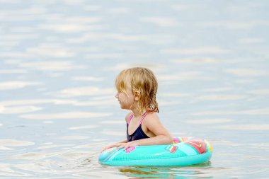Şişme yüzüklü küçük bir kız denizde banyo yapar ve yüzer..