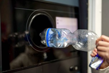 A woman returns plastic bottles to a plastic recycling machine. clipart