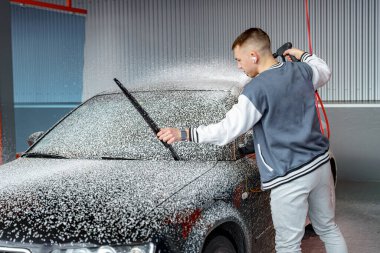 Bir şoför arabayı yıkadıktan sonra tazyikli suyla şampuanlandırır..