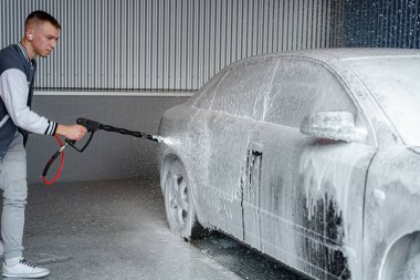 Bir adam araba yıkama yerindeki kiri temizlemek için köpük sürer..