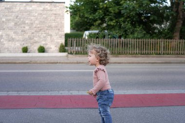 Küçük bir kız kaldırımda durur ve yola bakar..
