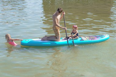 Çocuklarıyla birlikte genç bir baba denizde şişme bir tahta sürüyor..