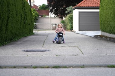 Küçük bir kız sokakta çocuk motosikleti sürüyor..