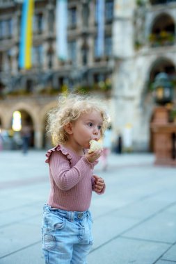 Küçük kıvırcık saçlı bir kız şehirde ekmek yiyor..
