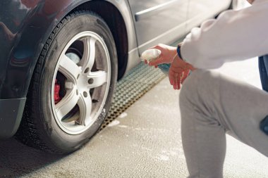 Sürücü yüksek basınçlı bir araba yıkama makinesinde araba tekerleğini yıkar..