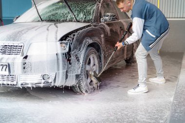 Sürücü yüksek basınçlı bir araba yıkama makinesinde araba tekerleğini yıkar..
