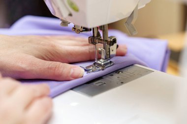 Dikiş makinesinde tekstil kumaşı işleniyor, iplik ve iğnelerin yakın çekimi..