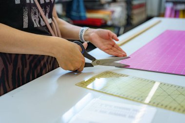 Bir kadın, fabrikada dikiş deseninin yanında elinde makas tutar..